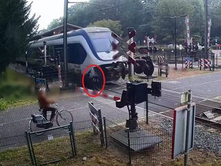 Vrouw loopt langs dichte spoorbomen, wordt op haar na niet geraakt door trein