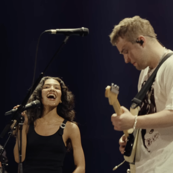 Olivia Dean singing beside Sam Fender as he plays guitar