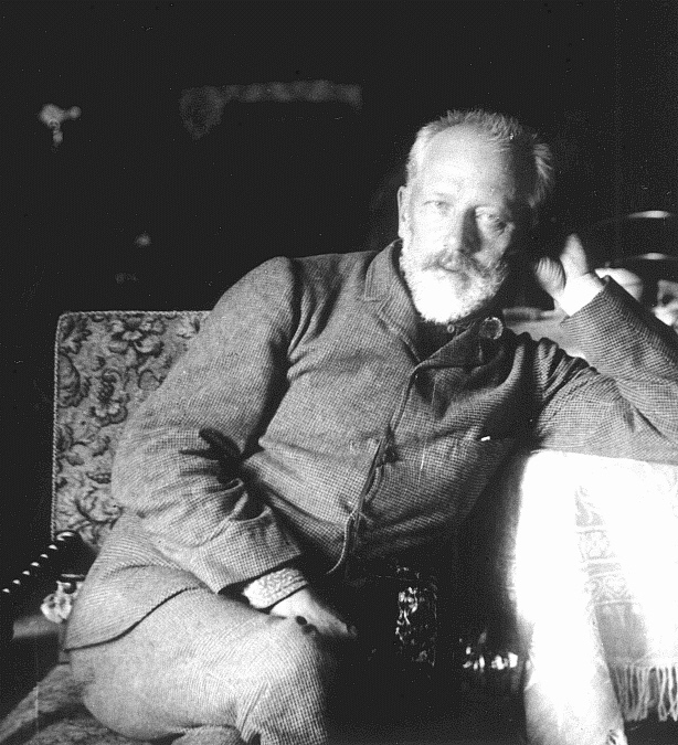 De componist Pjotr Iljitsj Tsjaikovski zit naast een tafel, leunt erop met één elleboog en kijkt in de camera