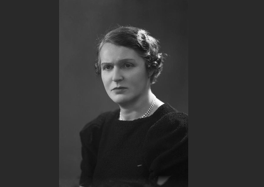 een zwart-wit portret van Germaine Tailleferre. Ze is een vrouw met een serieuze, vorsende blik. Ze draagt een parelketting.