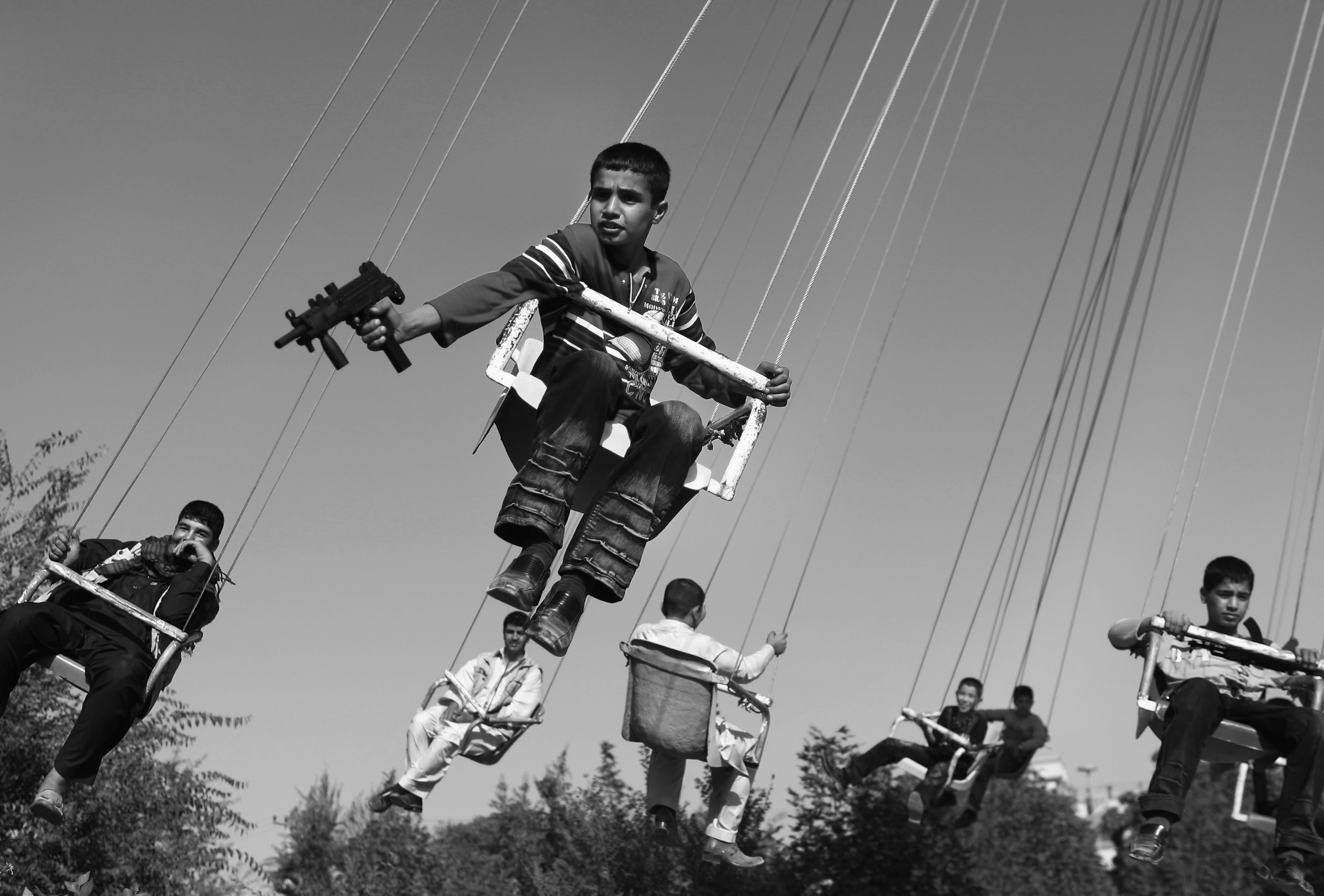 Een Afghaanse jongen houdt een speelgoedpistool vast terwijl hij geniet van een ritje in een draaimolen, Kabul, Afghanistan, september 2009