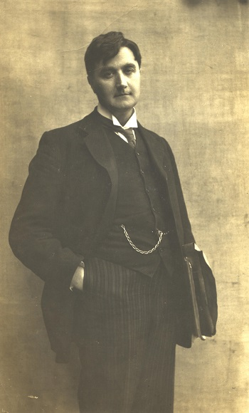 Ralph Vaughan Williams in een donker driedelig pak met een tas onder zijn arm en zijn hand in zijn broekzak